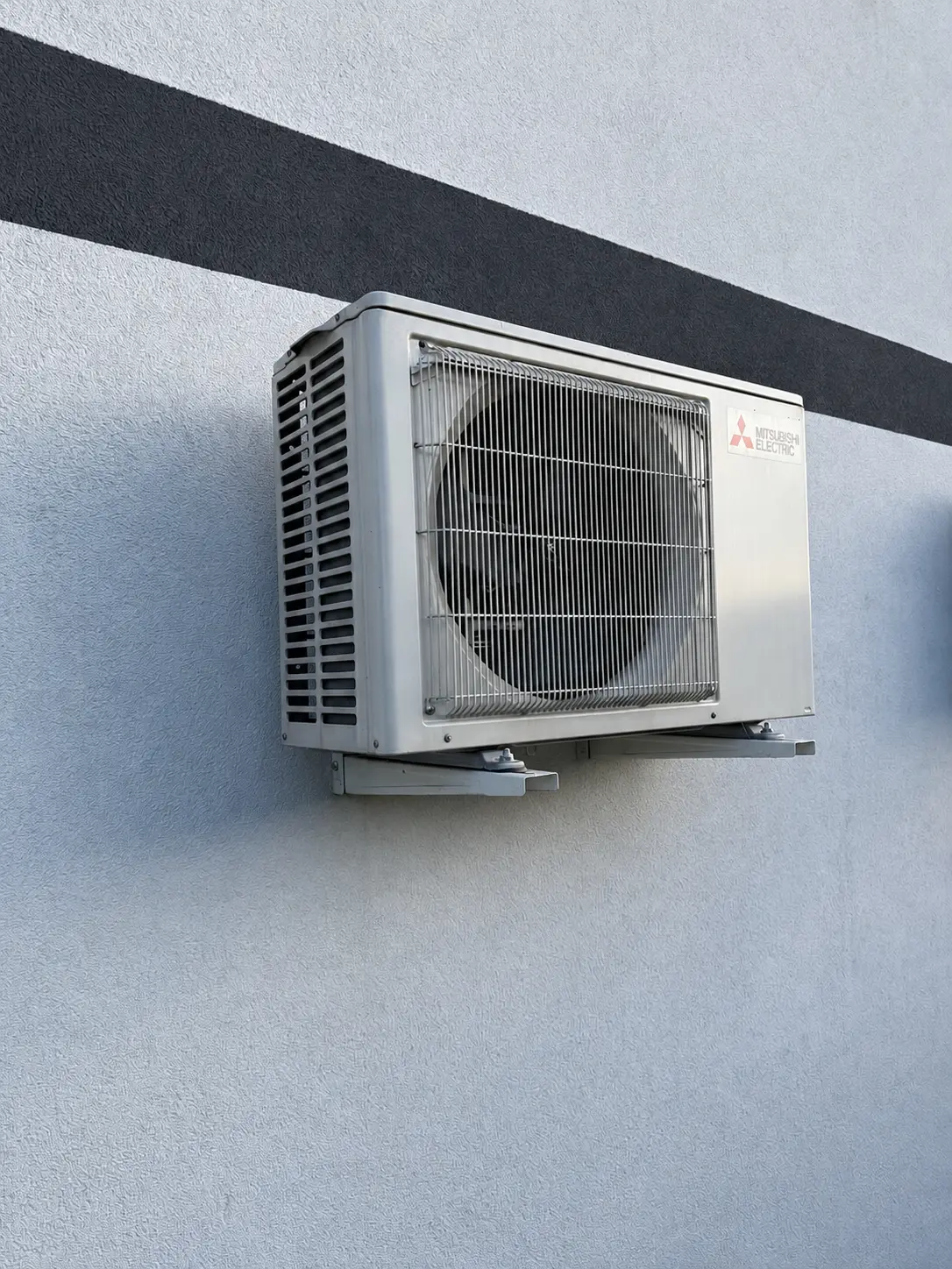 A bare white Mitsubishi Electric condenser unit mounted on a facade